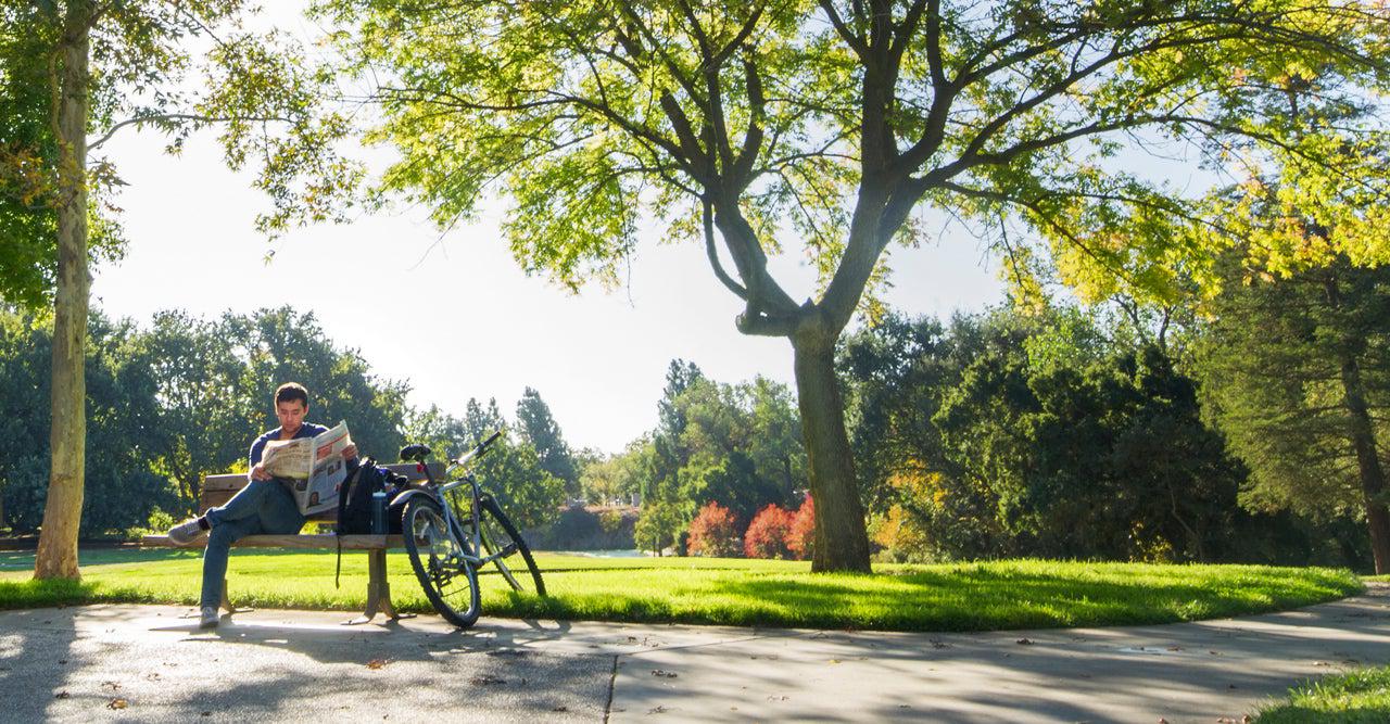 一个学生骑着自行车坐在长椅上读书. 