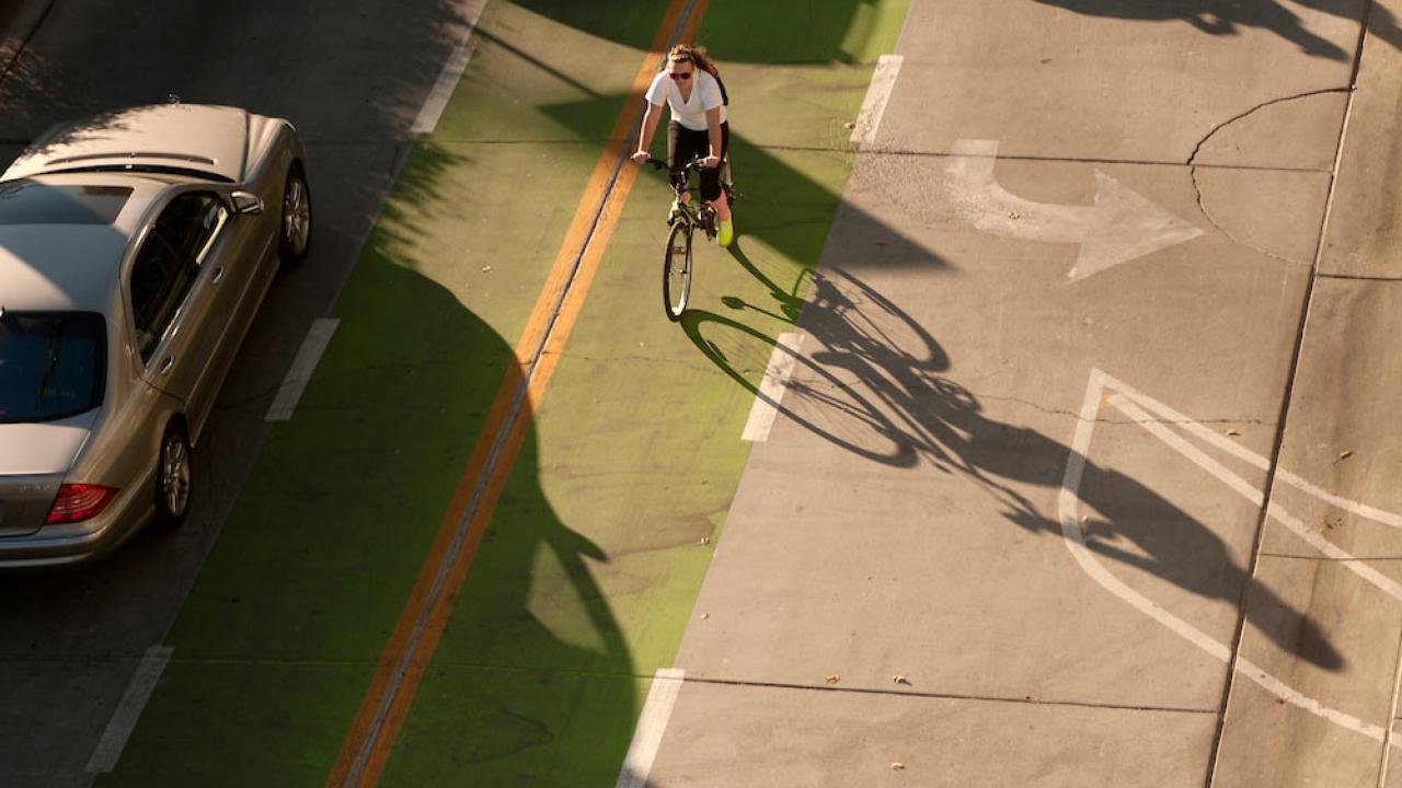 在澳门十大电子游戏大全，一名女学生骑着自行车穿过一条标记清晰的绿色自行车线，旁边是一辆汽车