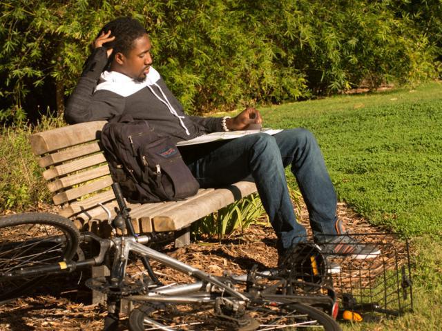 一个学生坐在树木园的长椅上学习 