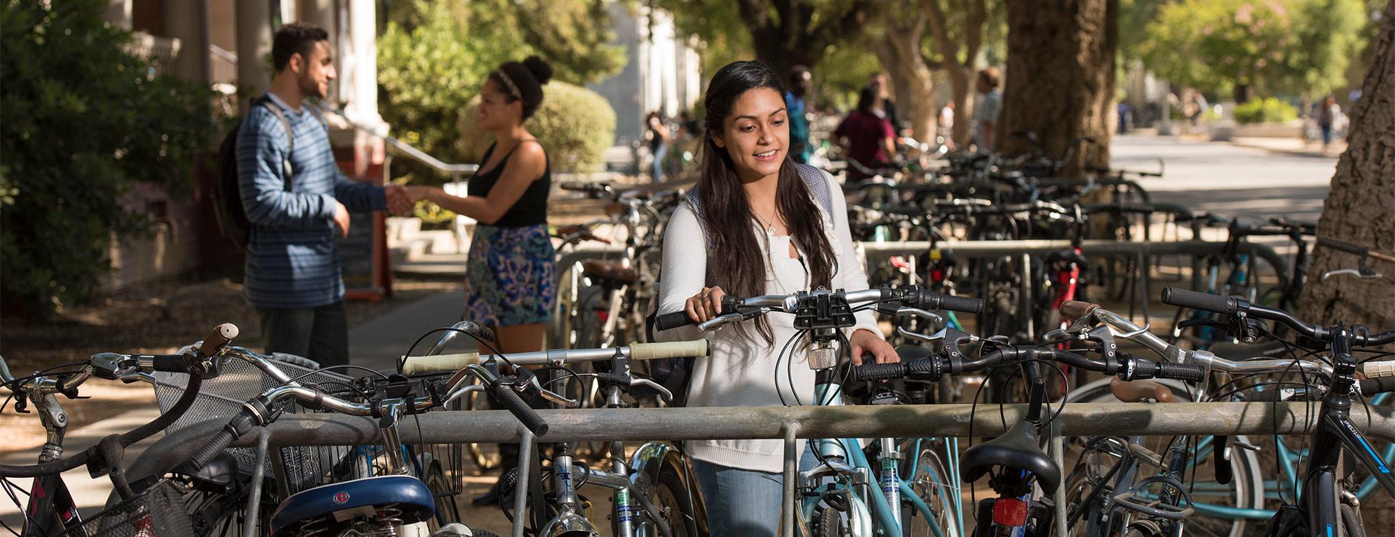 一个学生在放满自行车的自行车架上给自行车开锁，两个学生在后面说话