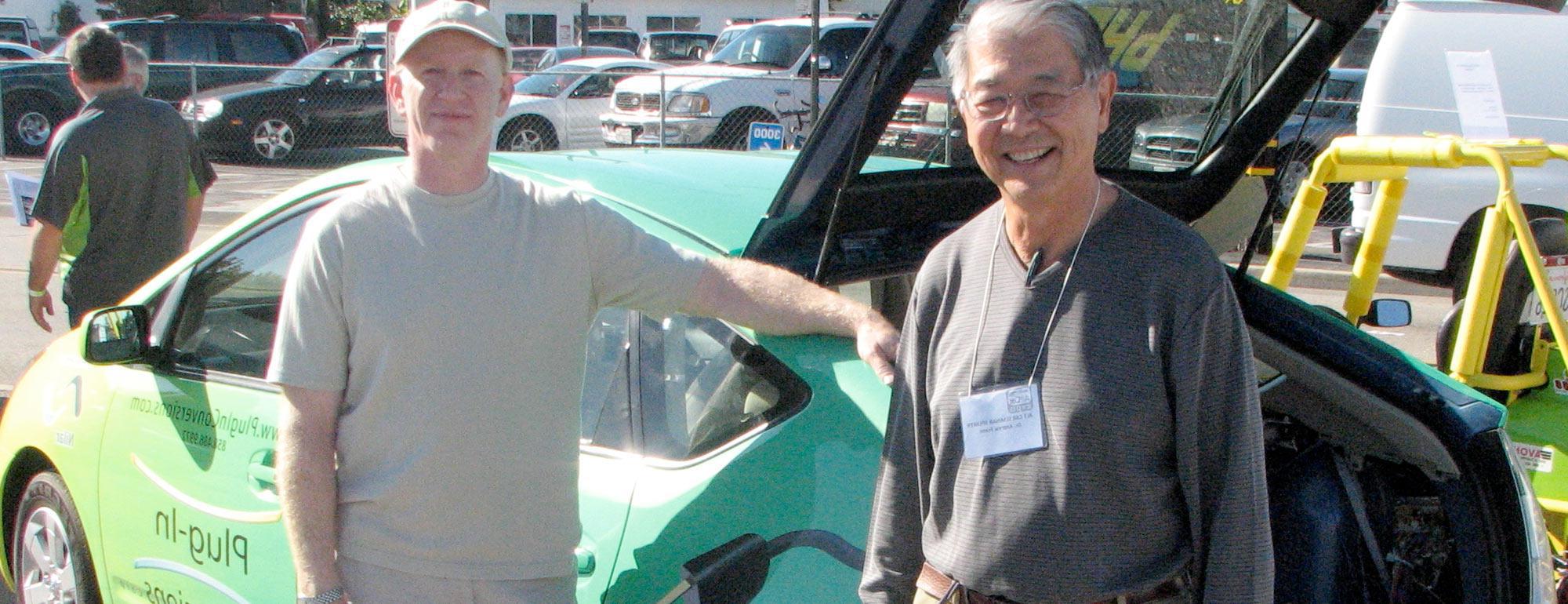 Two men pose next an electric car