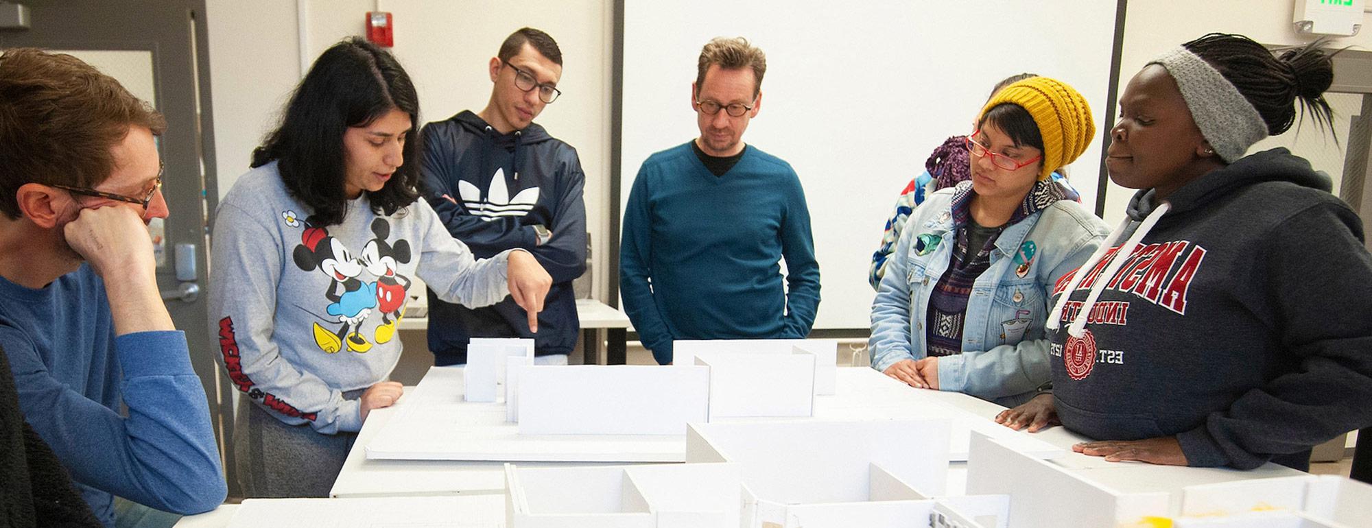 在设计课上，转学生们站在一个建筑模型周围