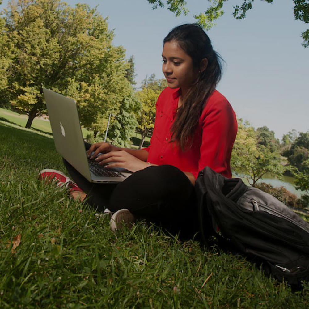 一名穿红色衣服的女学生在澳门十大电子游戏大全的院子里用笔记本电脑看书