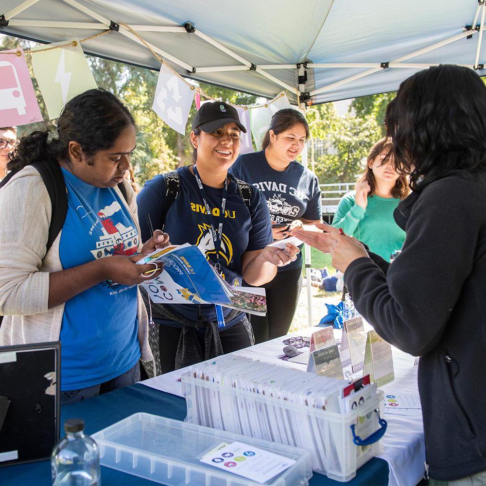 students receiving health information outdoors at a table in a tent