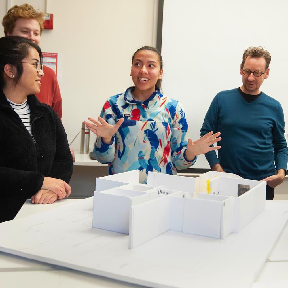 three students and a professor looking at a model of a building in a design class.